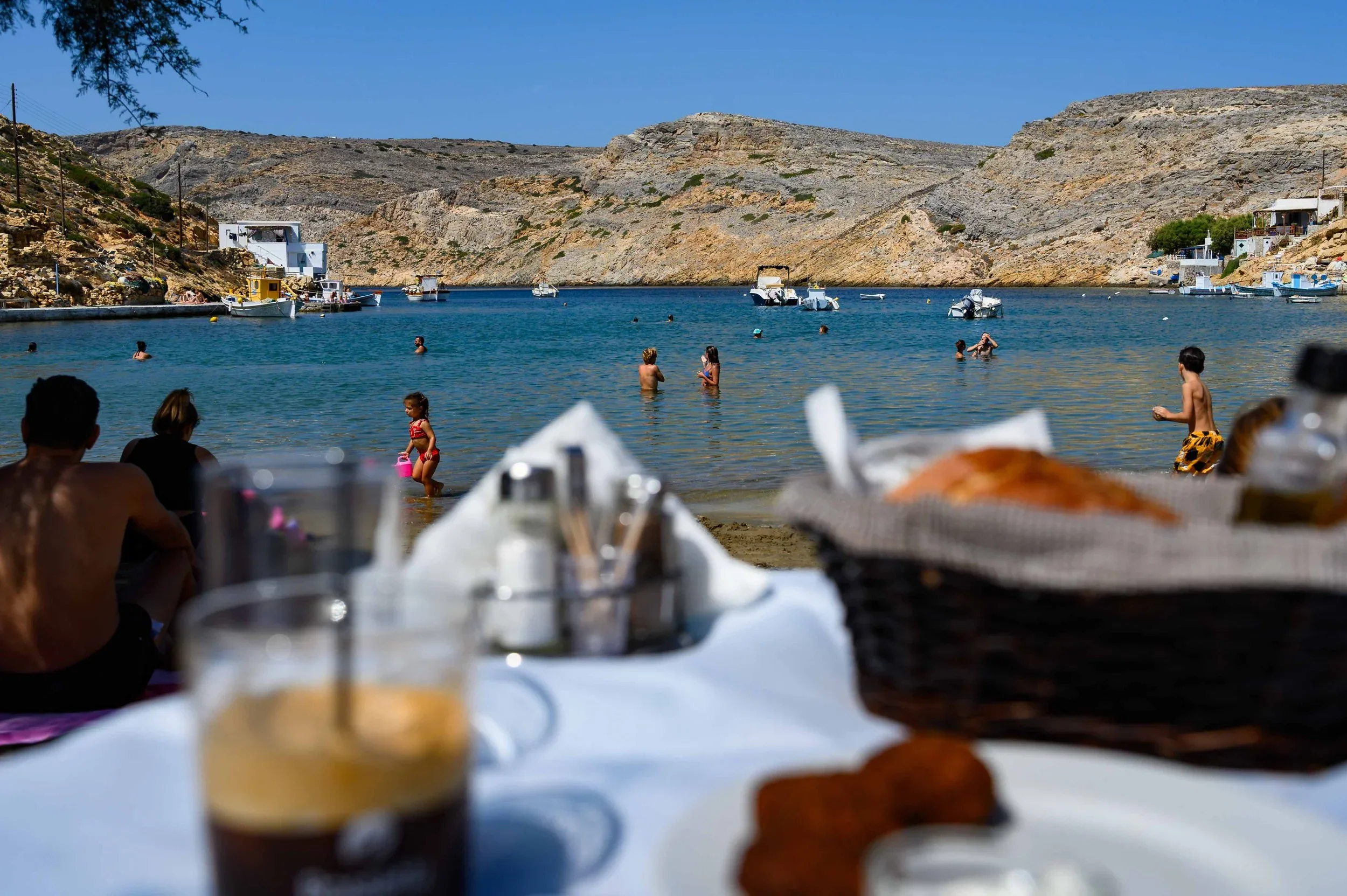 A table on the sand at Cheronissos, looking out over the bay to fishing boats and swimmers