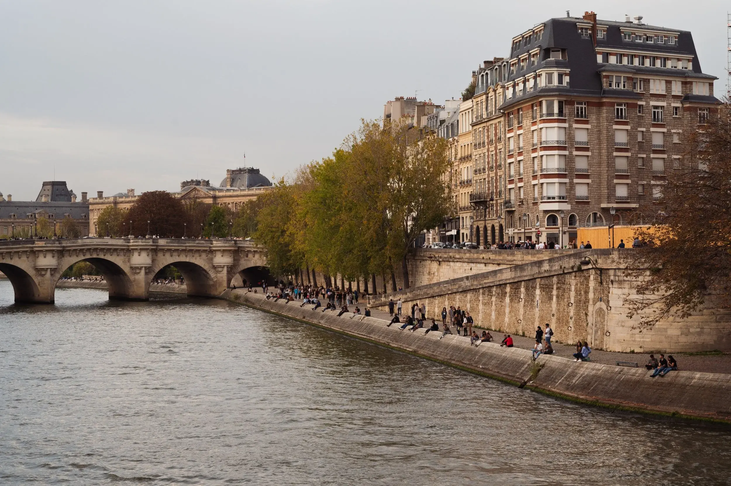 The Seine at the Pont Neuf in autumn, people sitting along the quay below the buildings