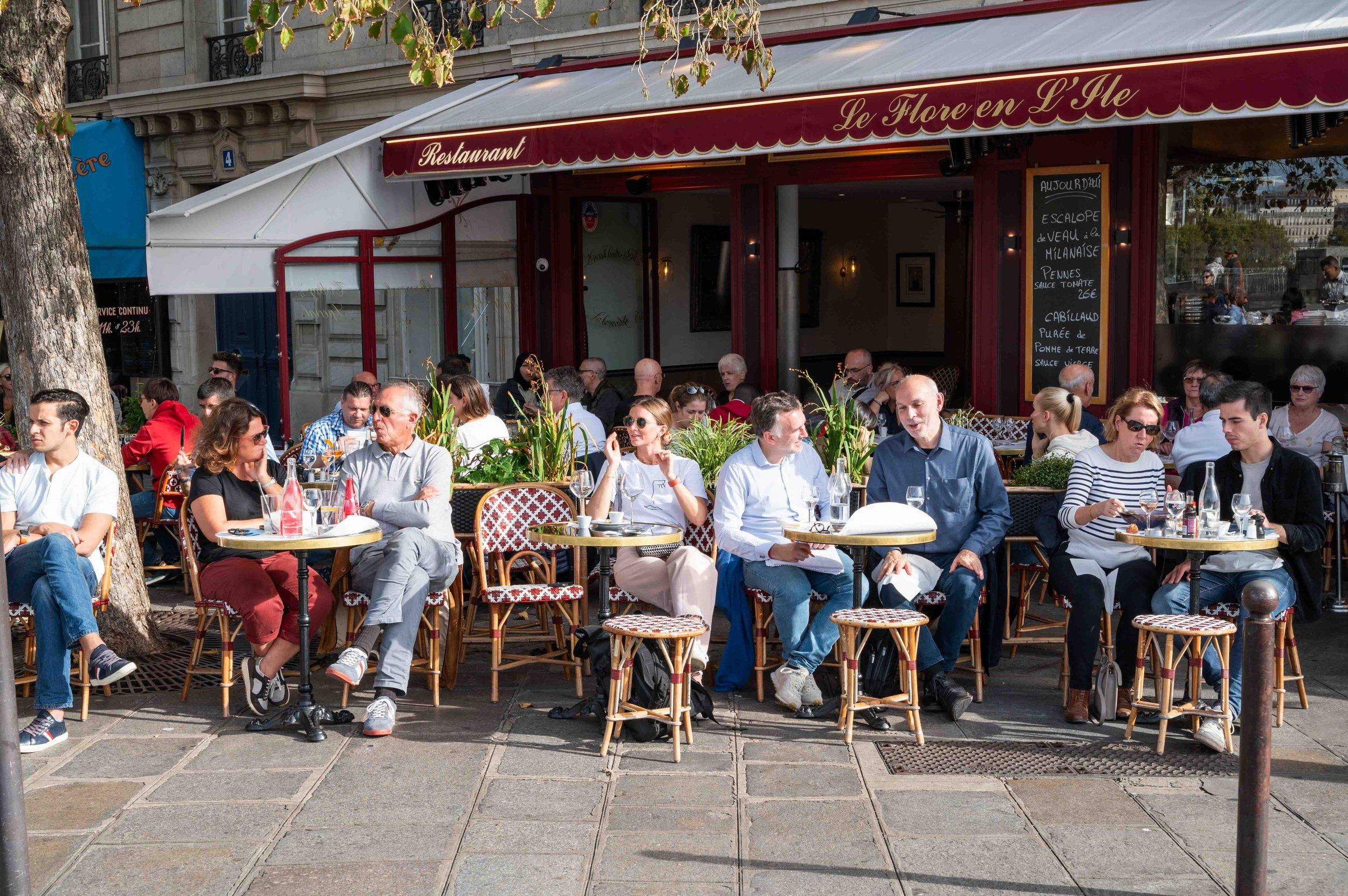 The busy pavement terrace of Le Flore en l'Île under its red awning, the name lettered across the front